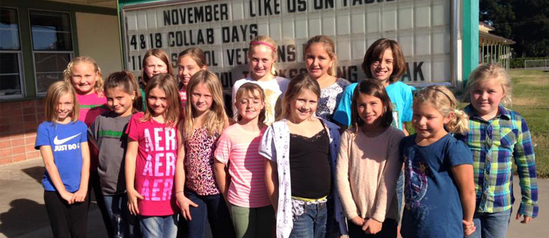 Group of young students smiling for the camera in front of the school